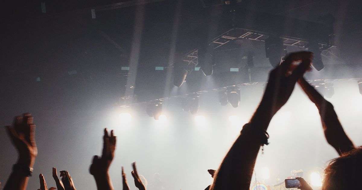Concert crowd with raised hands under stage lights, representing event cancellation insurance