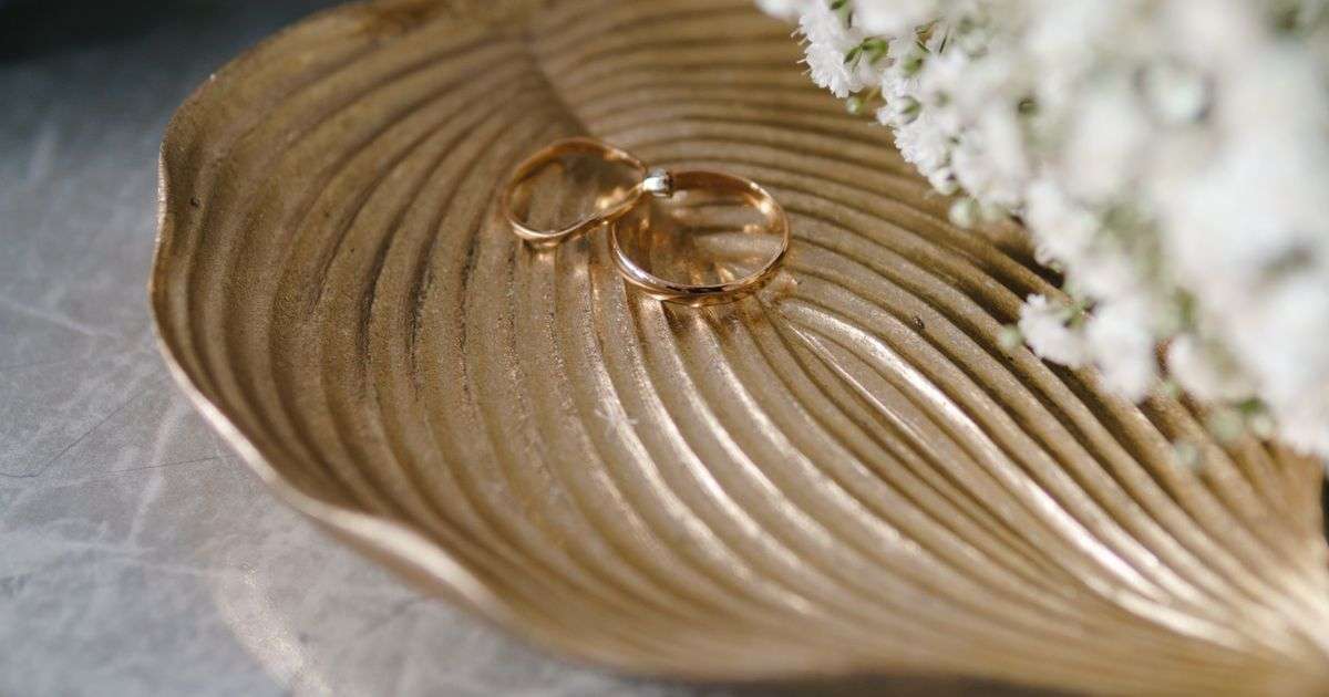 Wedding rings on a gold leaf plate beside white flowers, representing wedding insurance